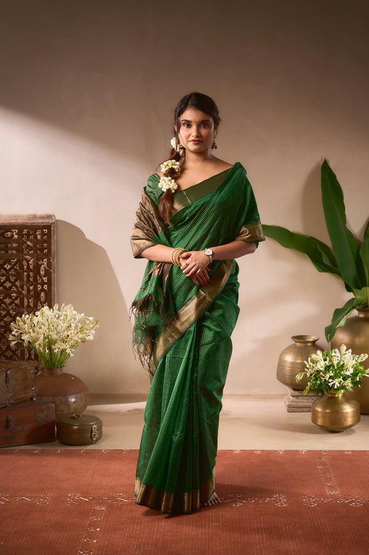 Woman in a green saree standing in a decorated room with plants and decorative items.