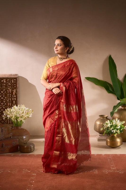 Woman in a red saree standing in a decorated room with plants and decorative items.
