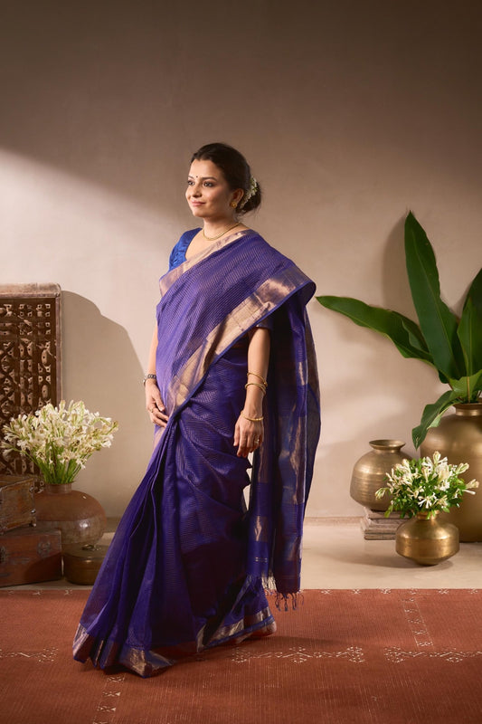 Woman in a blue saree standing in a decorated room with plants and vases.