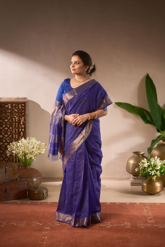 Woman in a blue saree standing in a room with decorative elements.