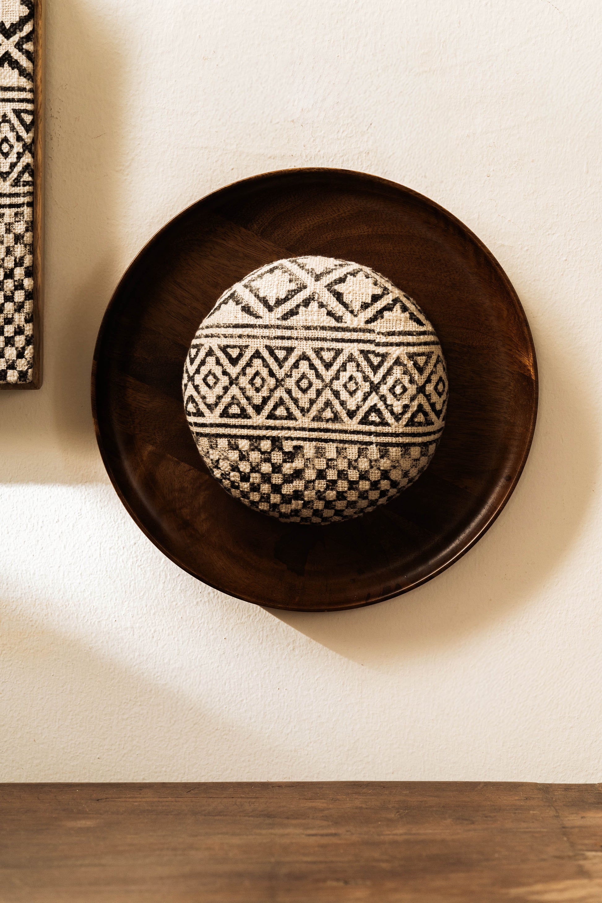 Two pieces of wall decor, one framed rectangular artwork and one circular framed artwork, with black and white geometric patterns, displayed on a wall above a wooden table.