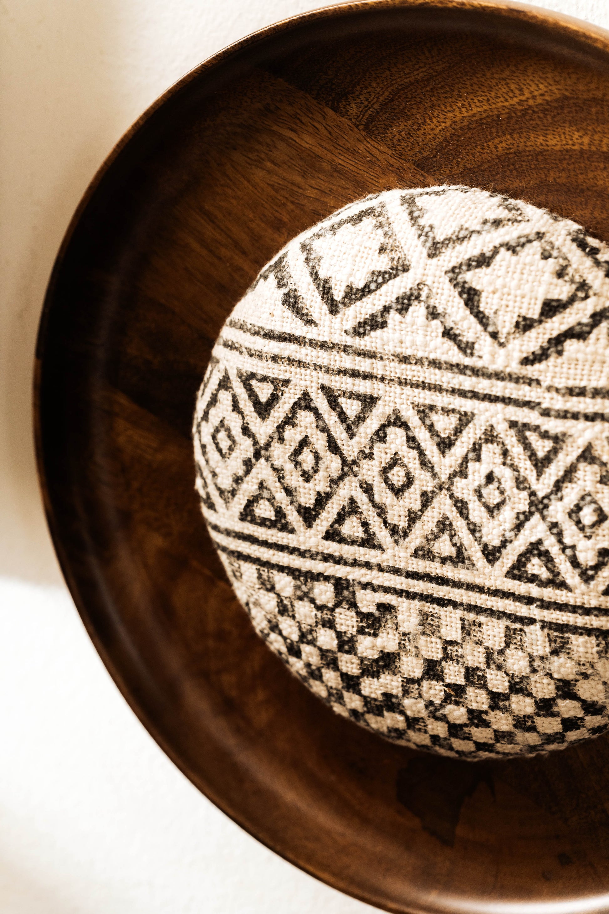 Two pieces of wall decor, one framed rectangular artwork and one circular framed artwork, with black and white geometric patterns, displayed on a wall above a wooden table.