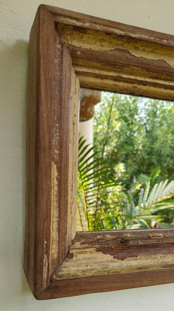 Wooden-framed mirror with a natural finish, reflecting green foliage.