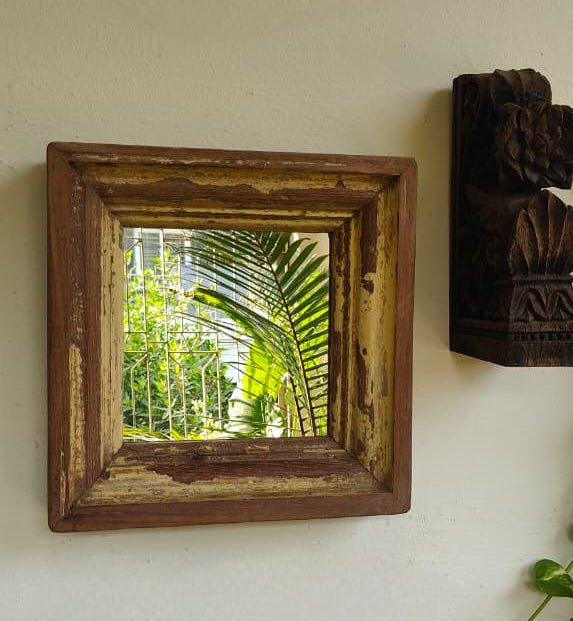 Wooden framed mirror on a wall with a view of greenery outside