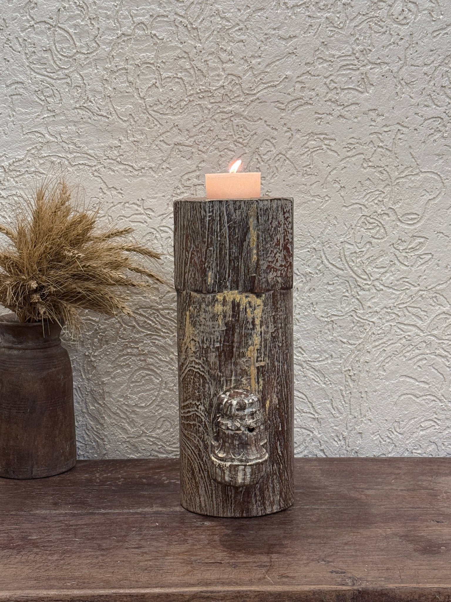 Decorative wooden candle holder with a face design on a textured wall.