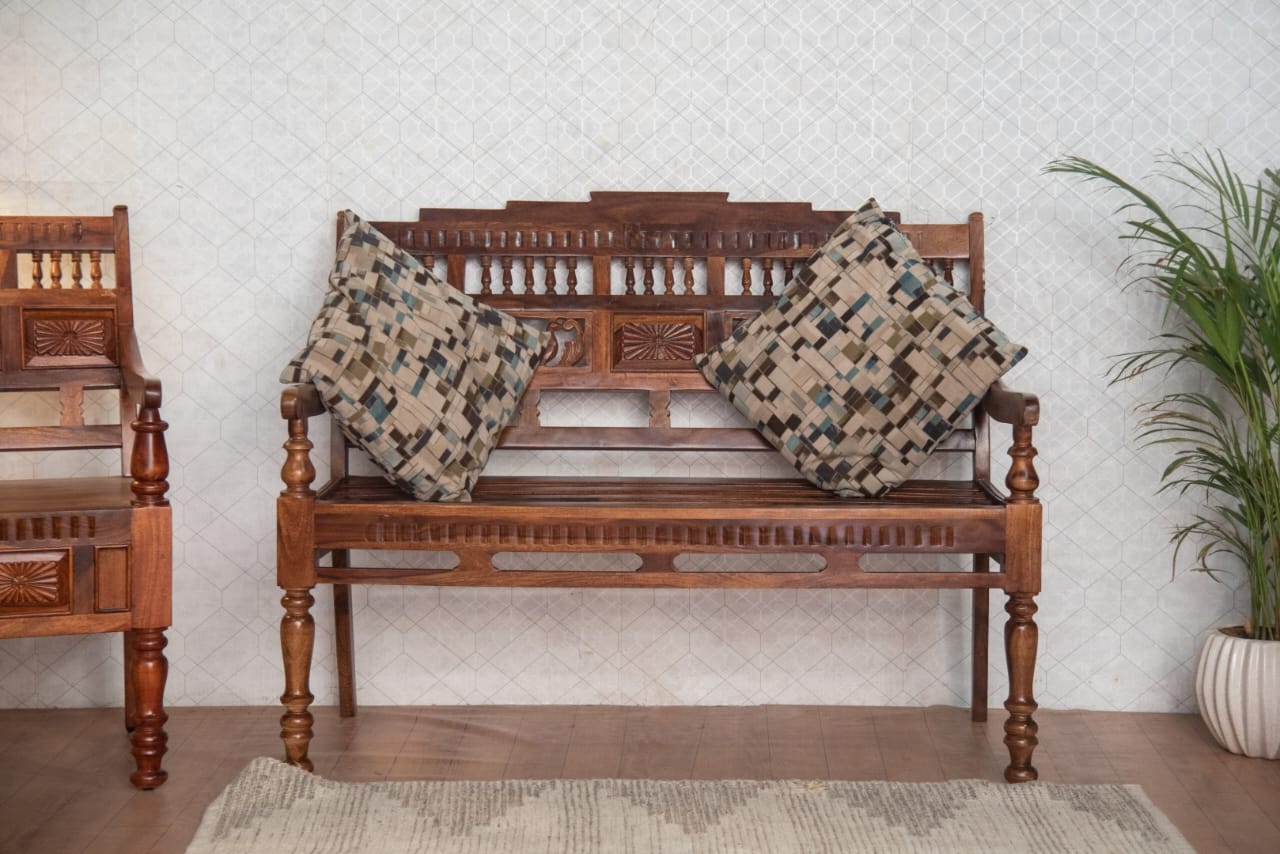 Wooden bench with intricate carvings and patterned cushions against a light wall.