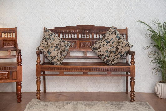 Wooden bench with intricate carvings and patterned cushions against a light wall.