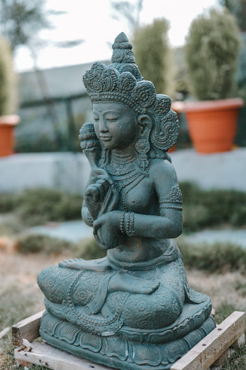 Green stone statue of a seated figure with intricate details in an outdoor setting.