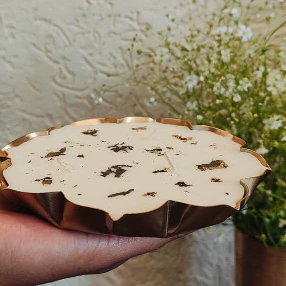 Hand holding a decorative item with a gold rim and white center against a floral background