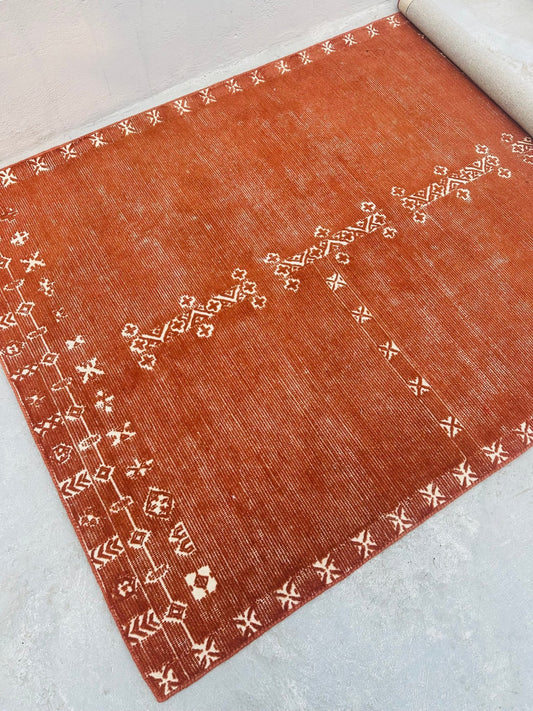 Reddish-brown rug with white geometric patterns on a light gray background