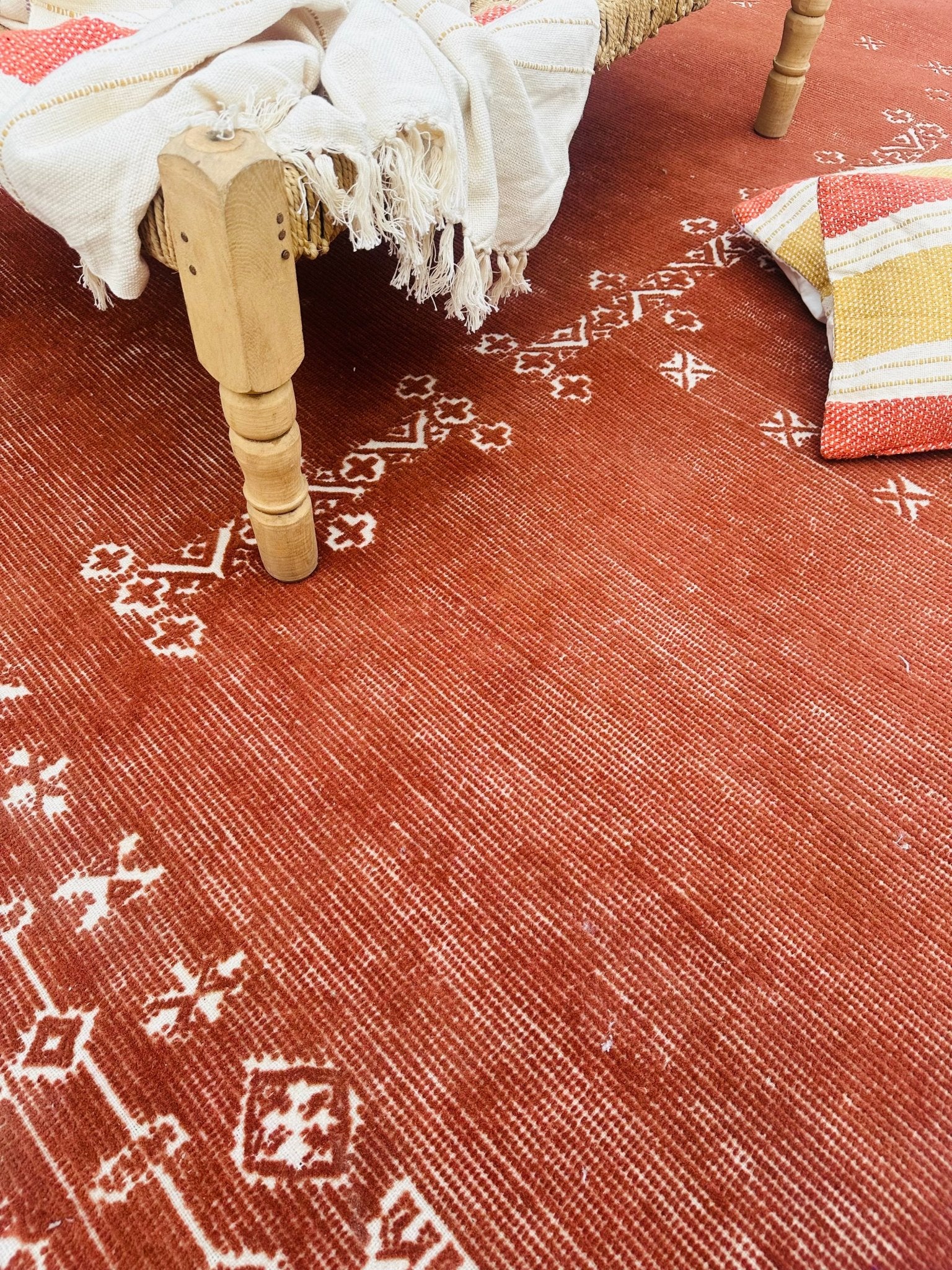 Close-up of a red patterned rug with a wooden stool and colorful cushions.