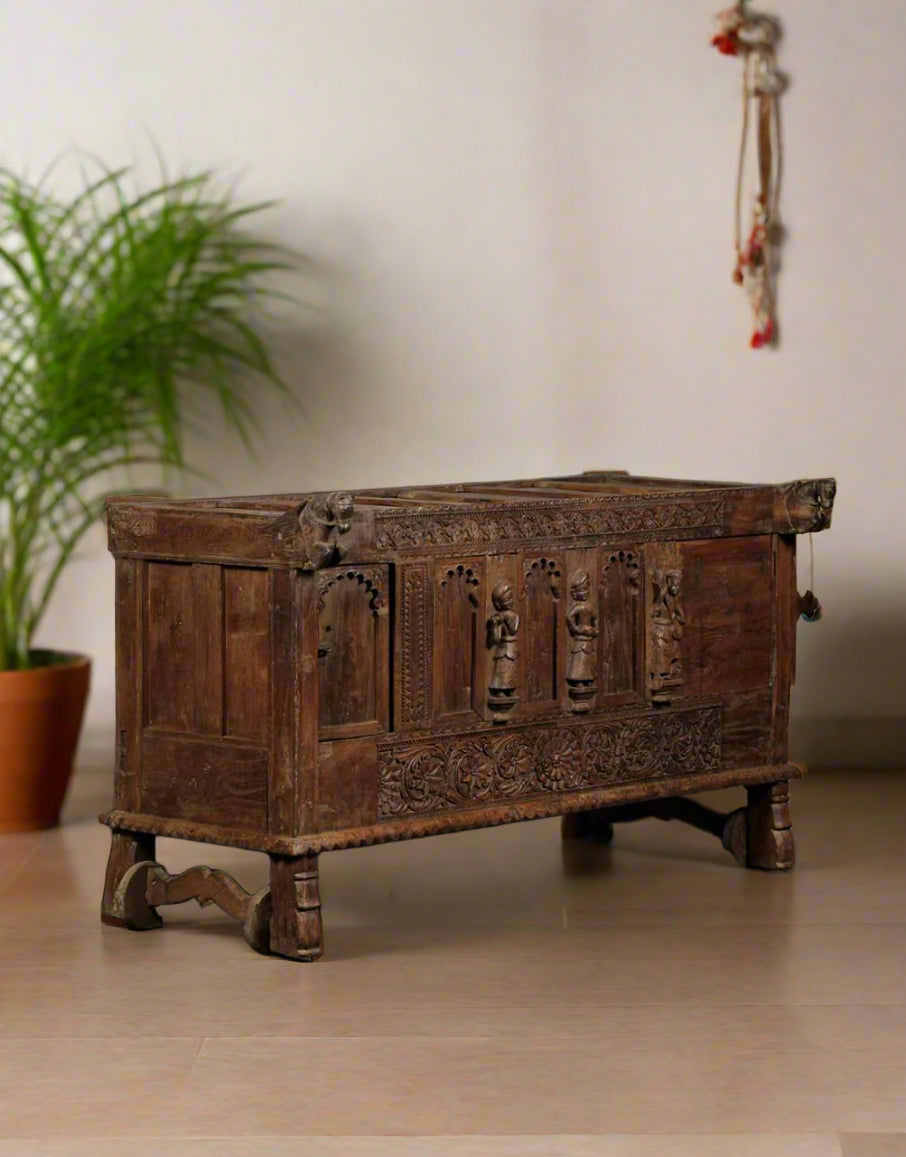 Vintage wooden chest with intricate carvings on a beige wall.