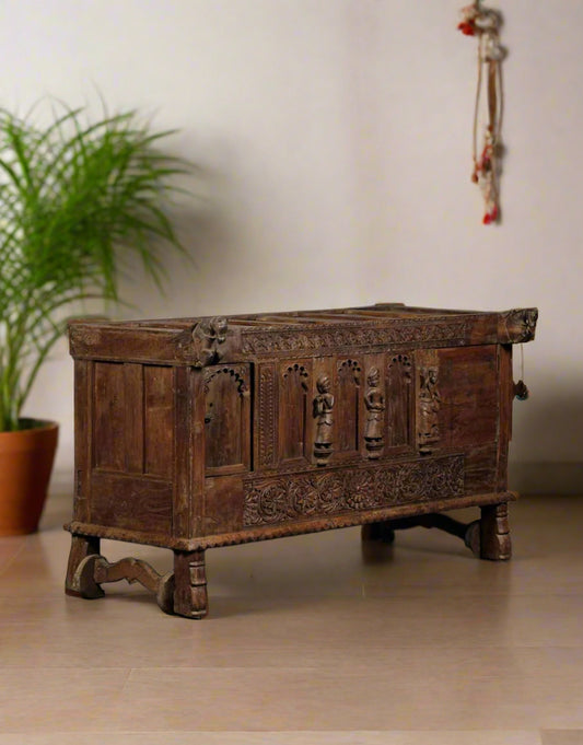 Vintage wooden chest with intricate carvings on a beige wall.