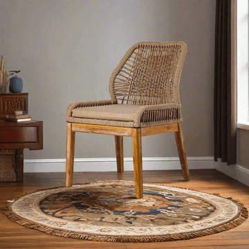 Wicker chair with cushion on a round patterned rug in a room with a wooden side table.