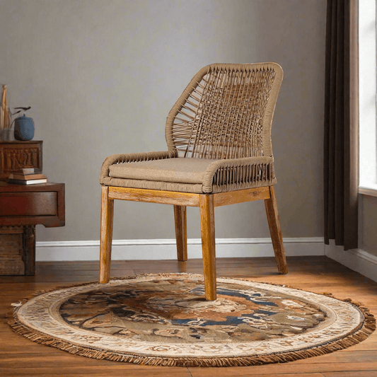 Wicker chair with cushion on a round patterned rug in a room with a wooden side table.