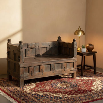 Wooden bench in a room with a lamp and decorative items on a patterned rug.