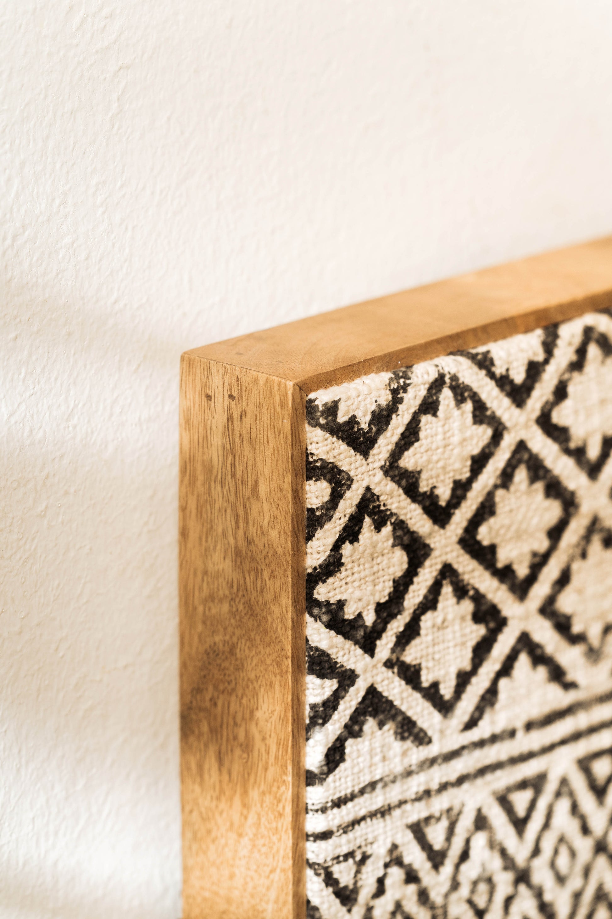 Two pieces of wall decor, one framed rectangular artwork and one circular framed artwork, with black and white geometric patterns, displayed on a wall above a wooden table.