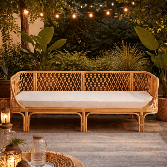 Wicker outdoor sofa with cushions in a garden setting with string lights and plants.