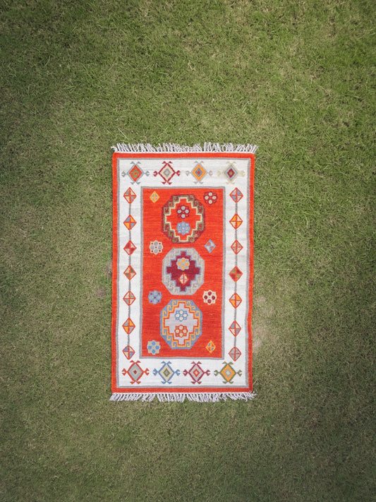 Close-up detail of handwoven geometric patterns in red, orange and white on heritage rug"
"Vibrant Heritage geometric rug displayed in modern living room setting