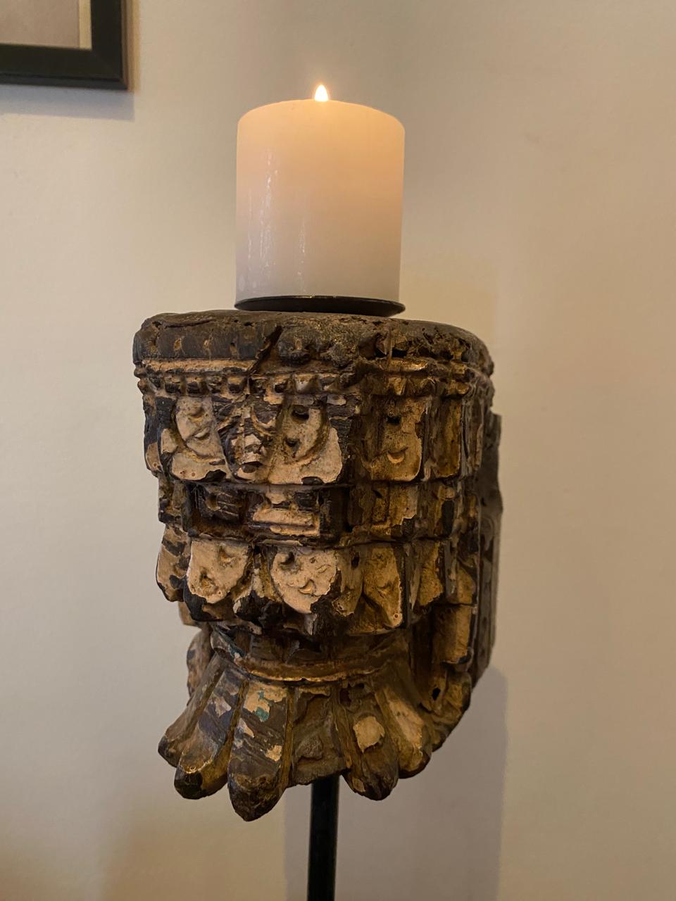 Decorative candle holder with a candle inside against a plain wall.