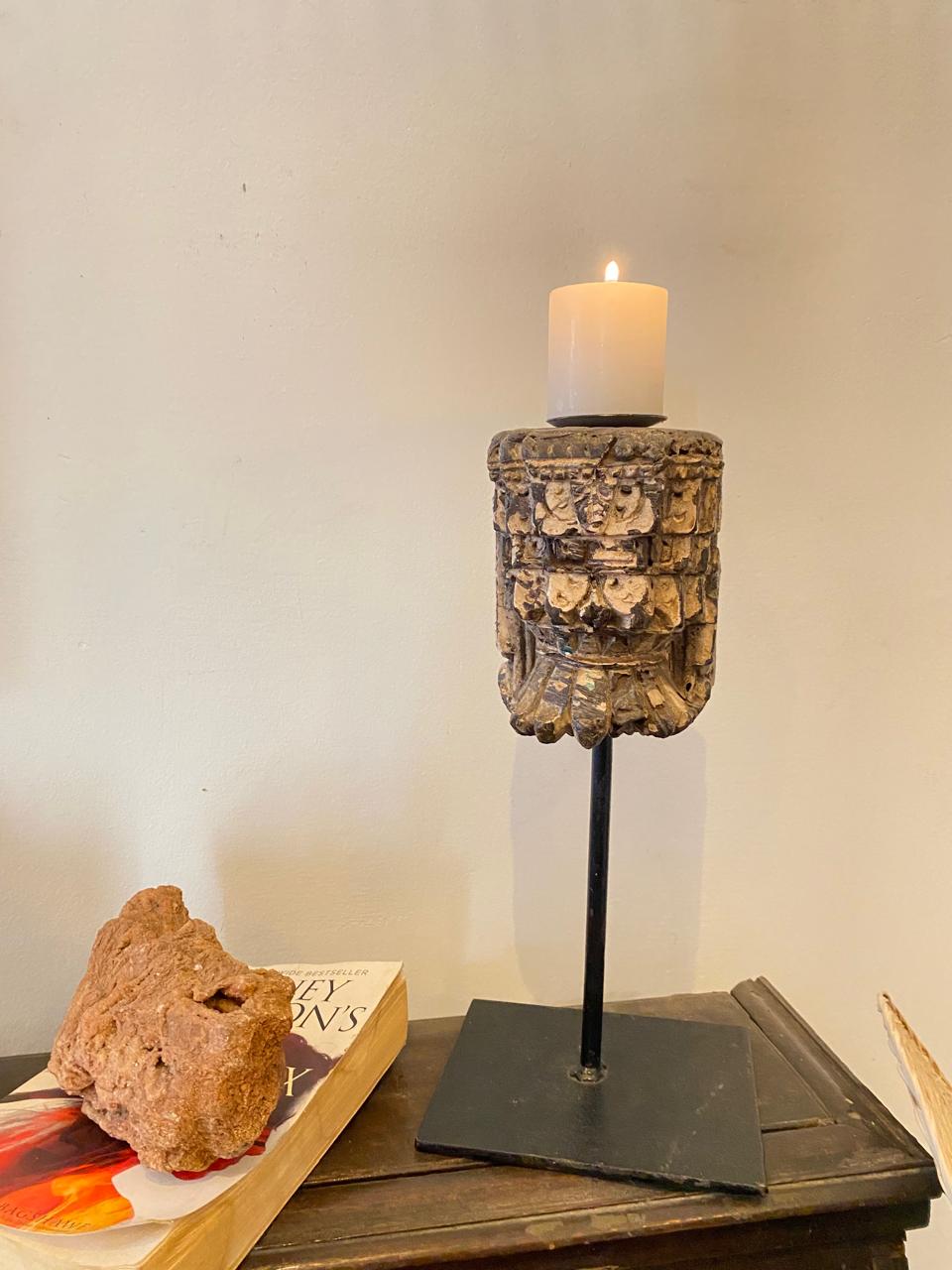Decorative candle holder with a candle on a wooden surface next to a book and rock.
