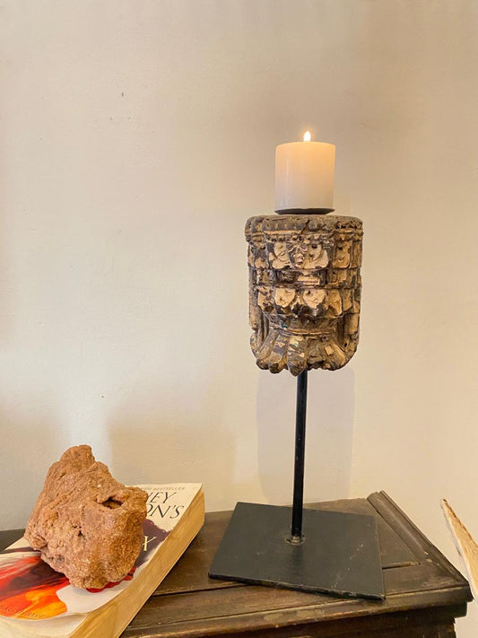 Decorative candle holder with a candle on a wooden surface next to a book and rock.