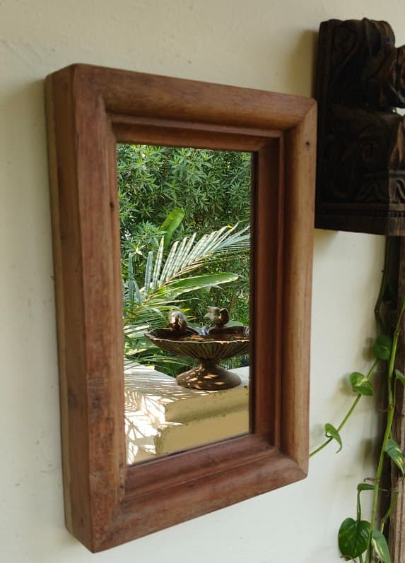 Wooden-framed mirror reflecting a garden scene with a fountain.