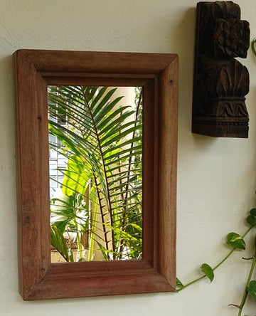 Wooden-framed mirror on a wall with decorative elements and plants.