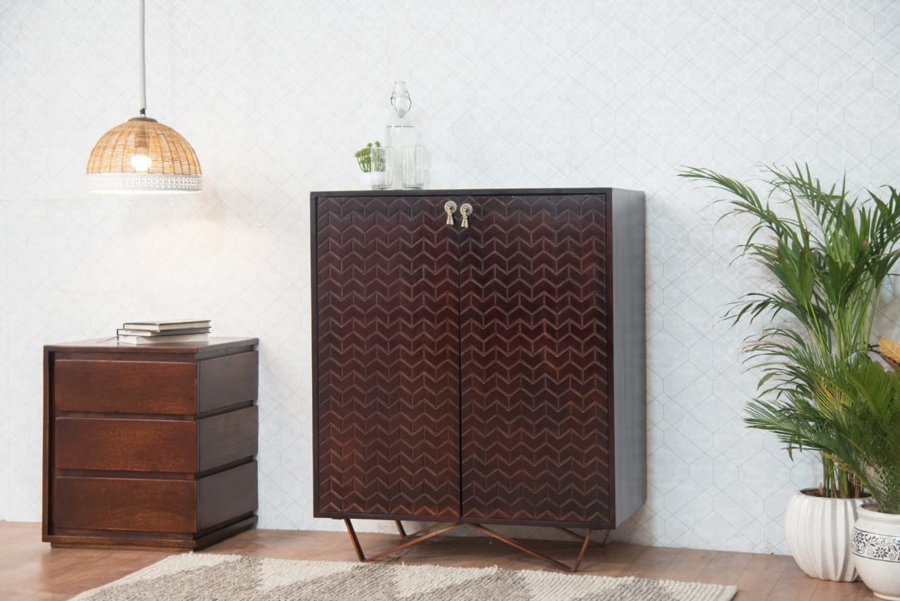 Wooden cabinet with chevron pattern in a room with a lamp, plant, and small table.