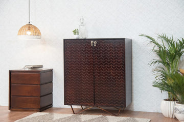 Wooden cabinet with chevron pattern in a room with a lamp, plant, and small table.