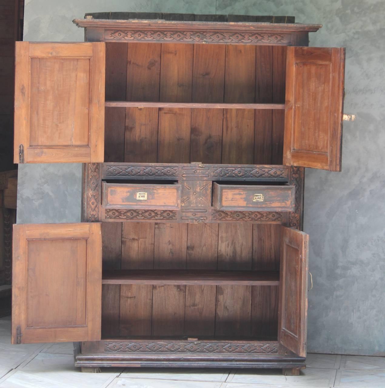 Wooden cabinet with open doors and carved details against a gray wall.