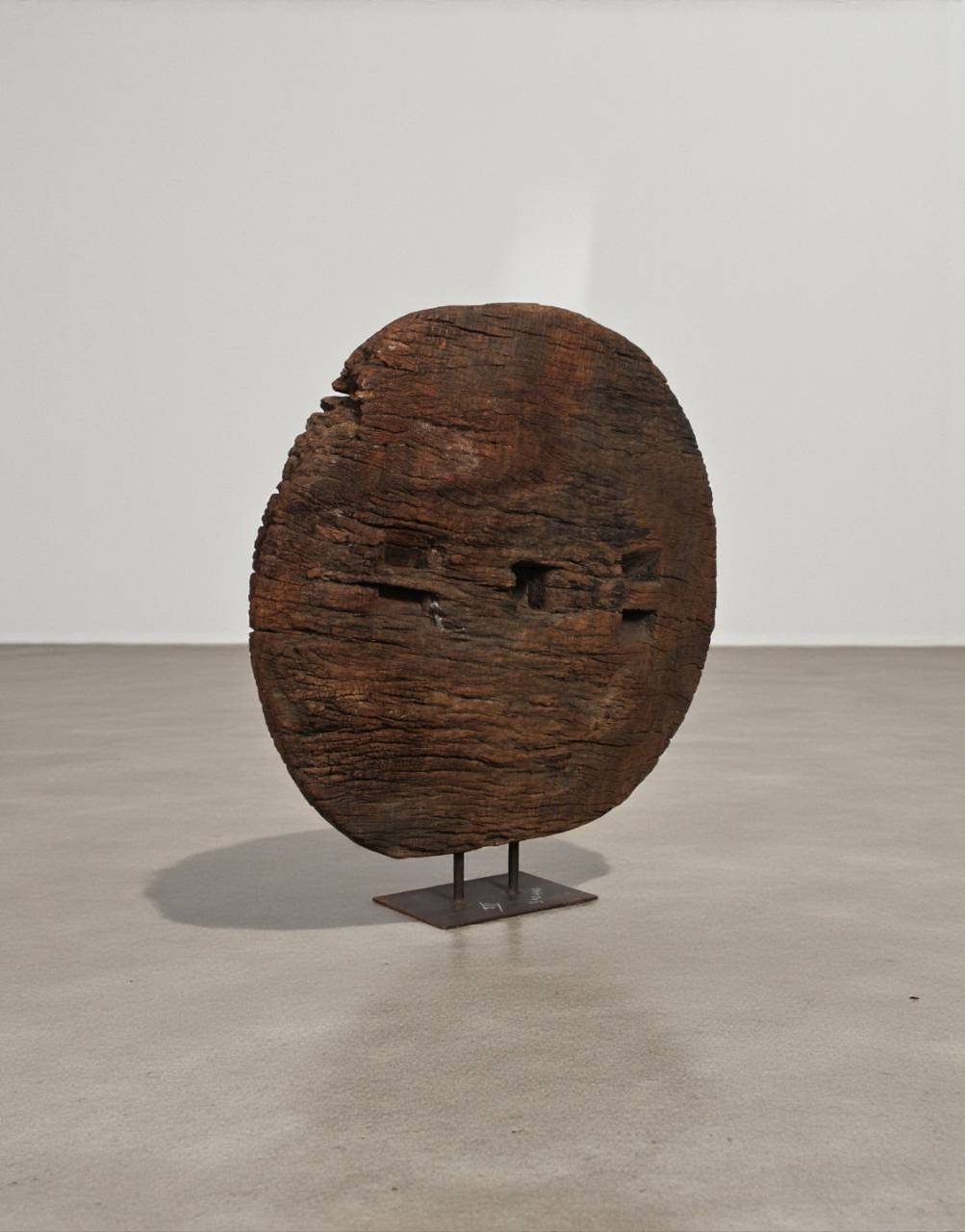 Wooden sculpture resembling a face on a stand against a plain background