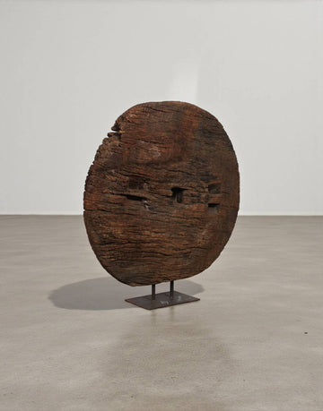 Wooden sculpture resembling a face on a stand against a plain background