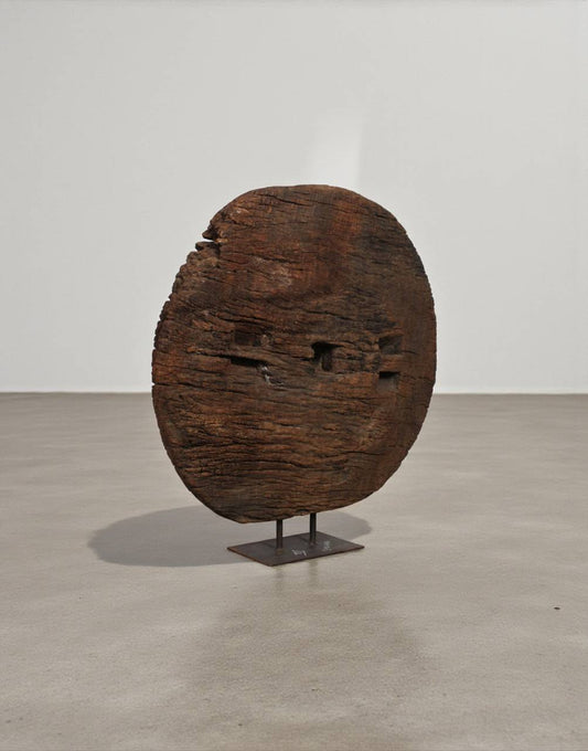 Wooden sculpture resembling a face on a stand against a plain background