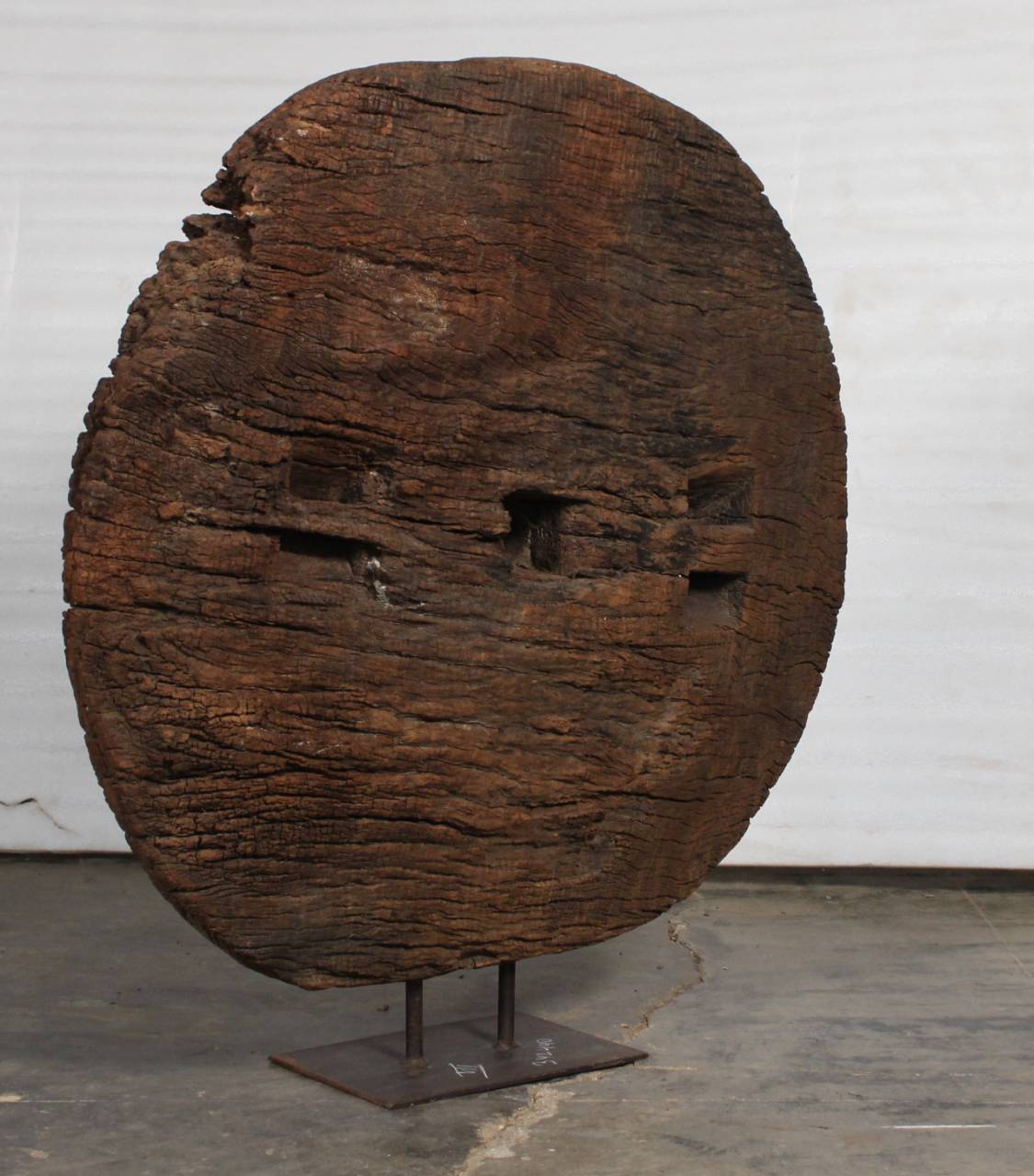 Wooden sculpture resembling a face on a stand against a white wall.