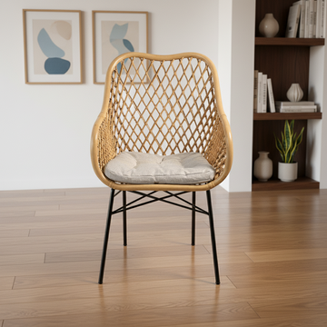 Wicker chair with a cushion on a wooden floor in a room with a bookshelf and framed pictures.