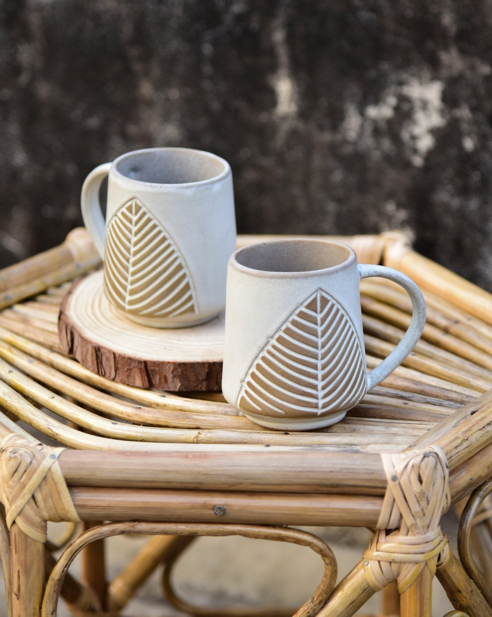 Two ceramic mugs with leaf patterns on a woven surface