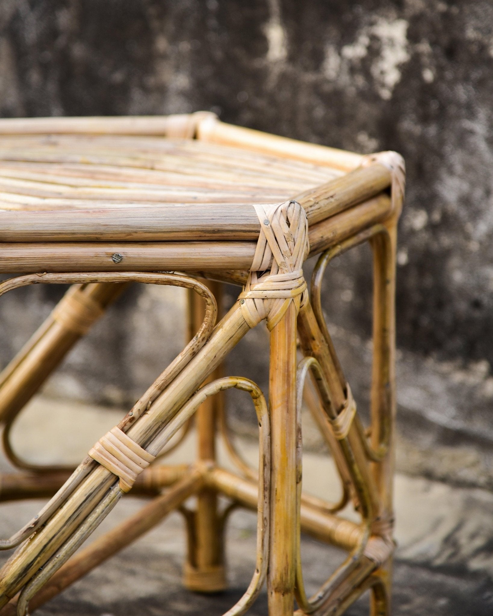 Rattan stool with woven seat and backrest against a textured wall.