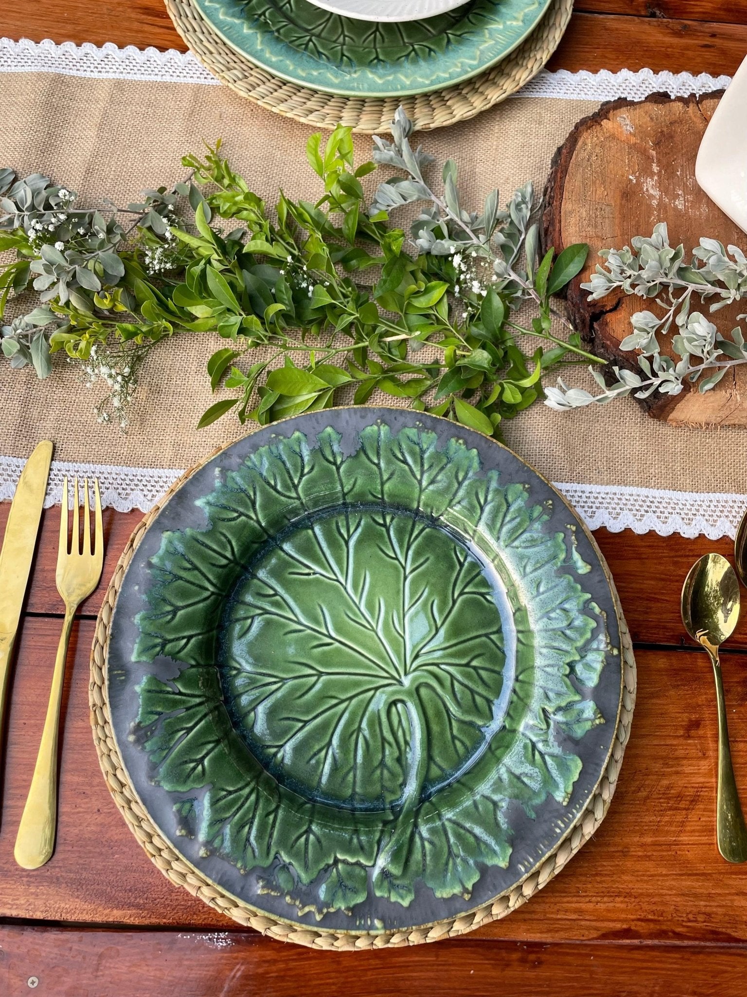 Decorative green ceramic plate with leaf pattern on a wooden table with greenery and cutlery.