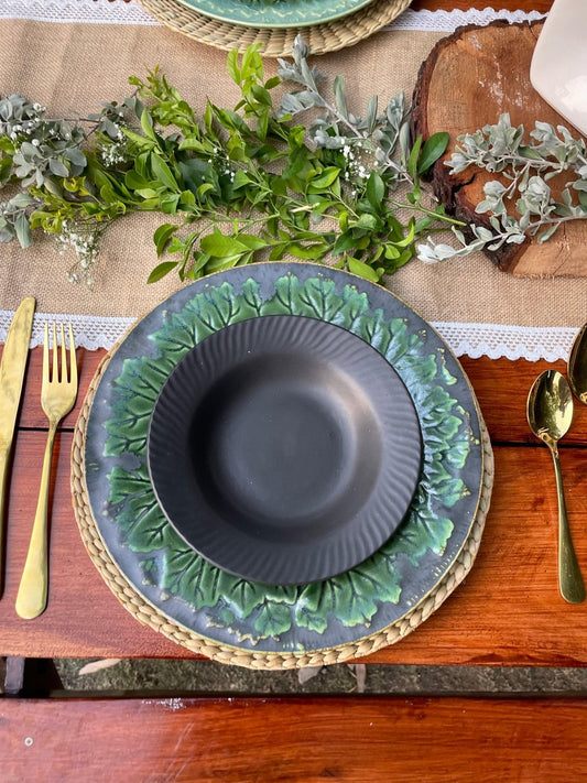 Decorative table setting with green and gold plates, silverware, and greenery on a wooden table.