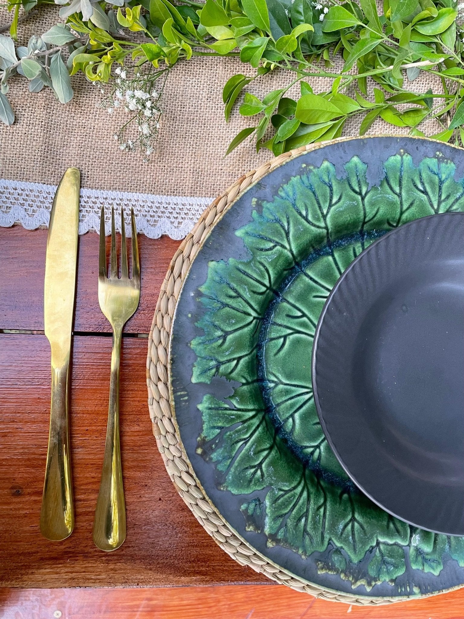 Green and blue ceramic plates with gold cutlery on a wooden table with greenery.