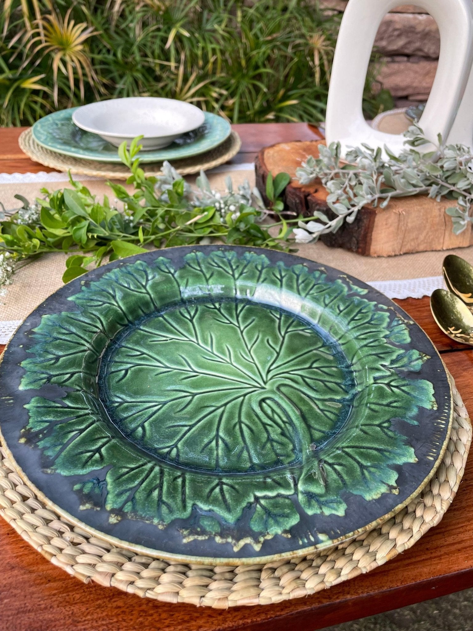 Green ceramic plate with leaf pattern on a wooden table with greenery