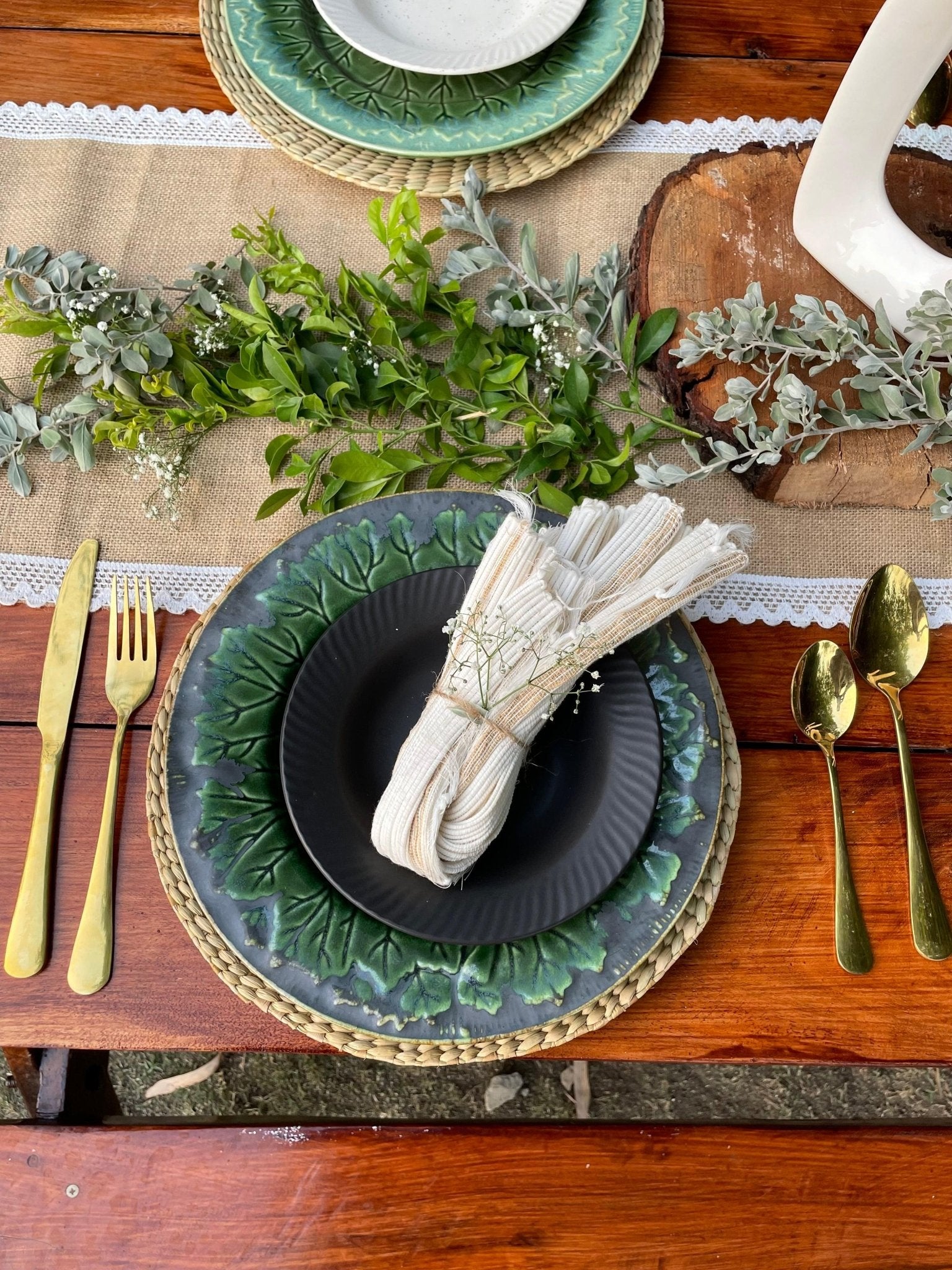 Elegant table setting with green plates, gold cutlery, and white napkin on a wooden table.