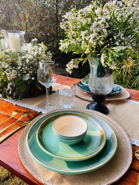 Table setting with green plates, white flowers, and candles outdoors.