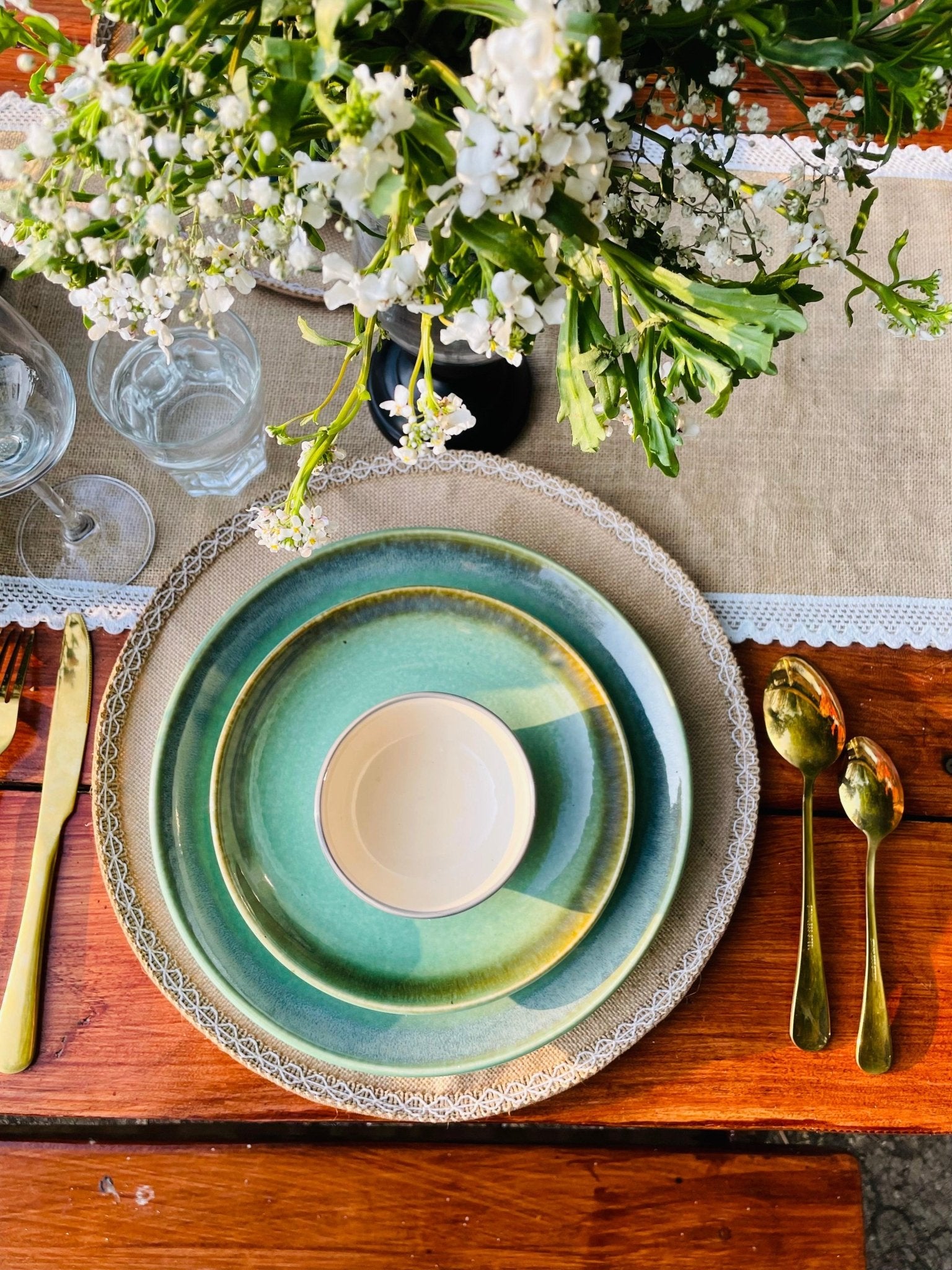 Table setting with green ceramic plates, gold cutlery, and white flowers on a wooden table.