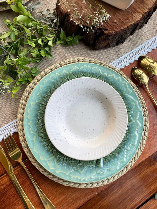 Teal ceramic plate with a white bowl on a wooden table with gold cutlery and greenery.