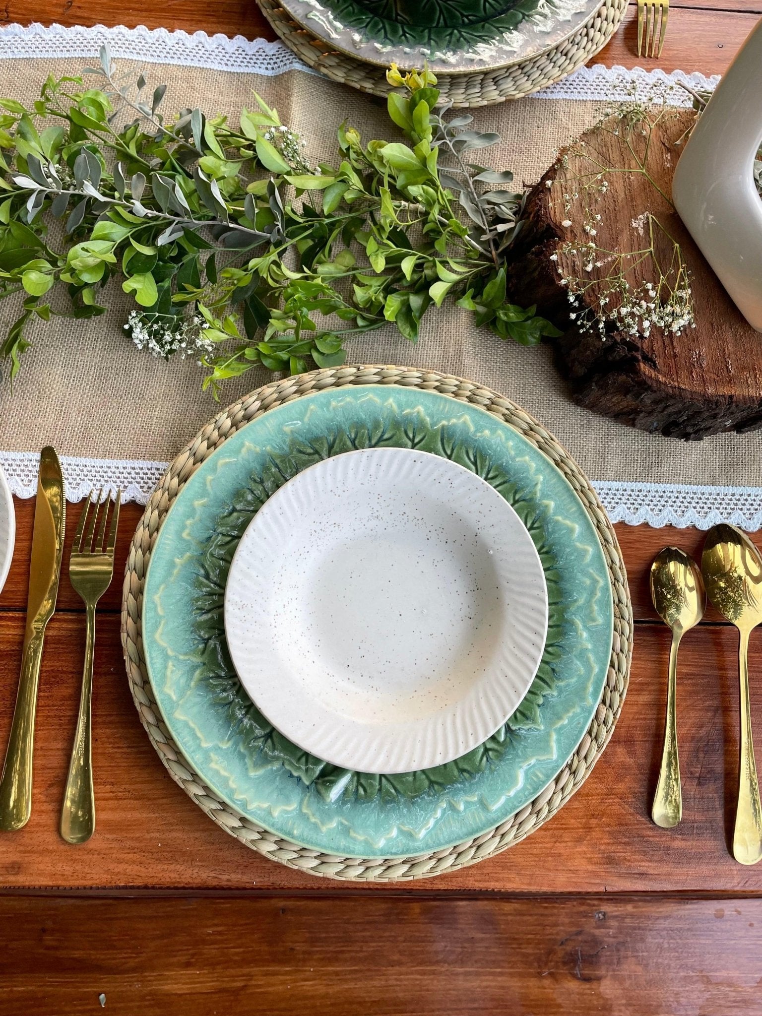 Table setting with green plates, gold cutlery, and a wooden log in the background.