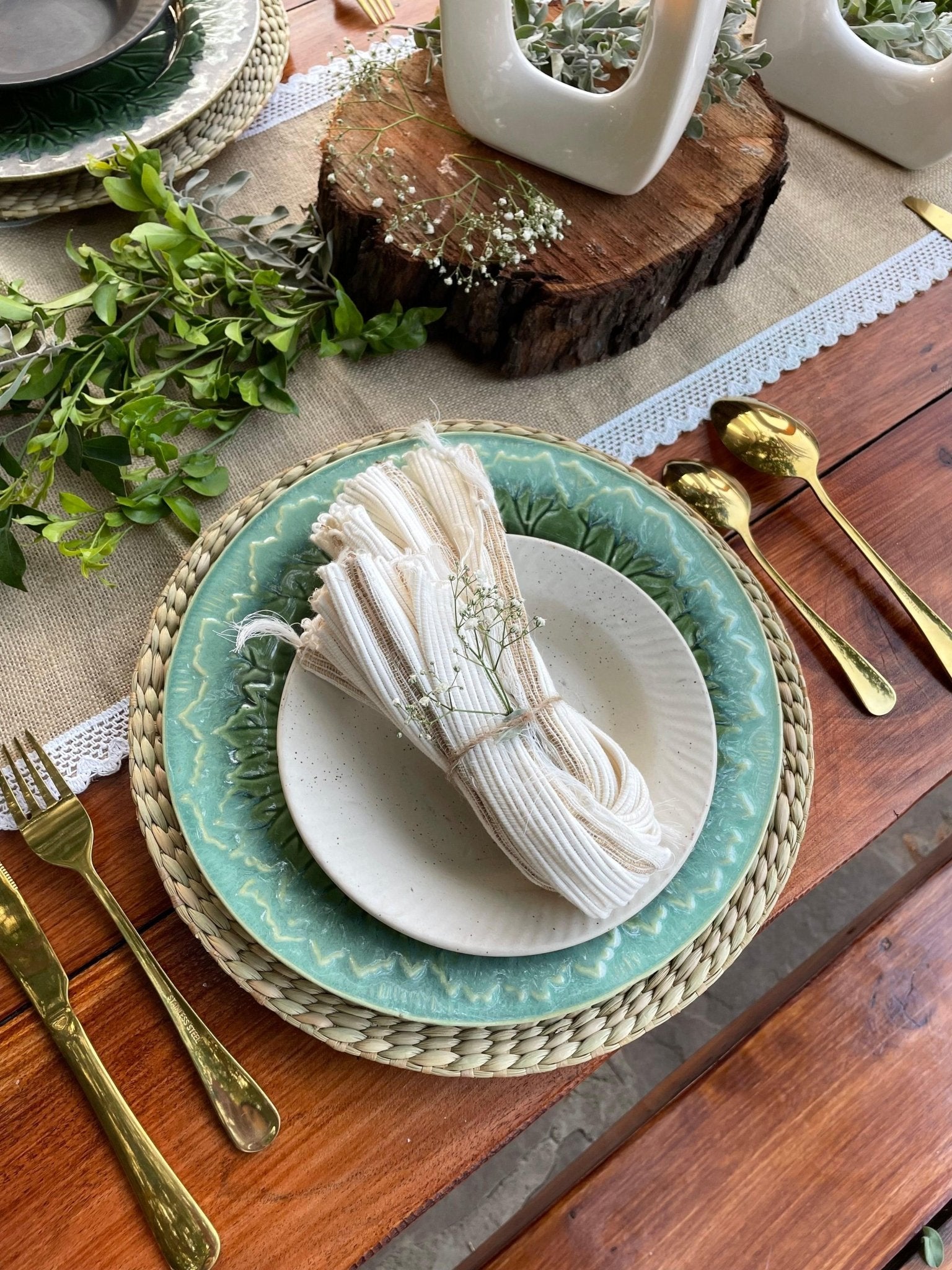 Decorative table setting with green plates, gold cutlery, and white napkins on a wooden table.