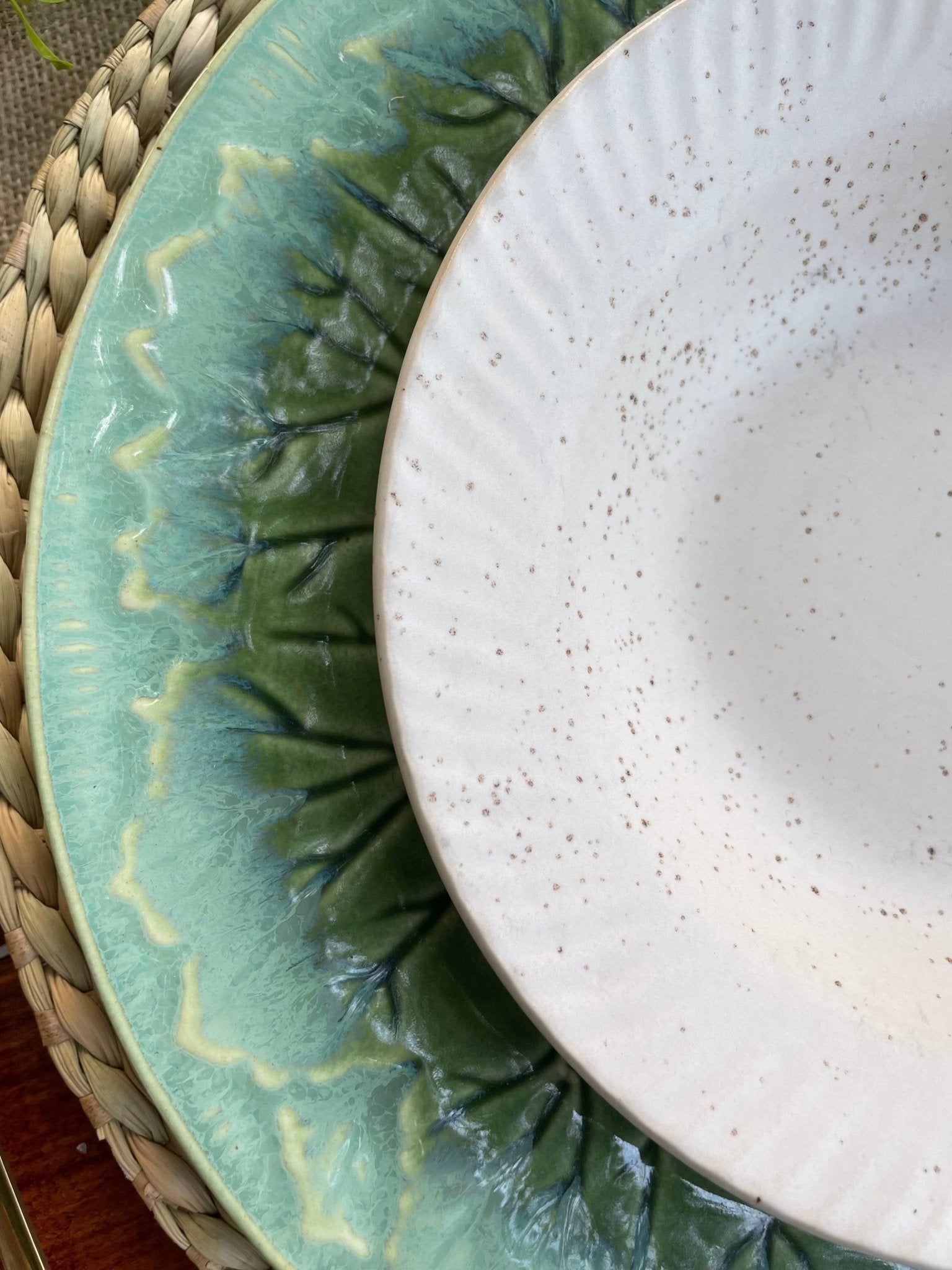 Two ceramic plates, one green with wavy pattern and one white speckled, on a woven surface.